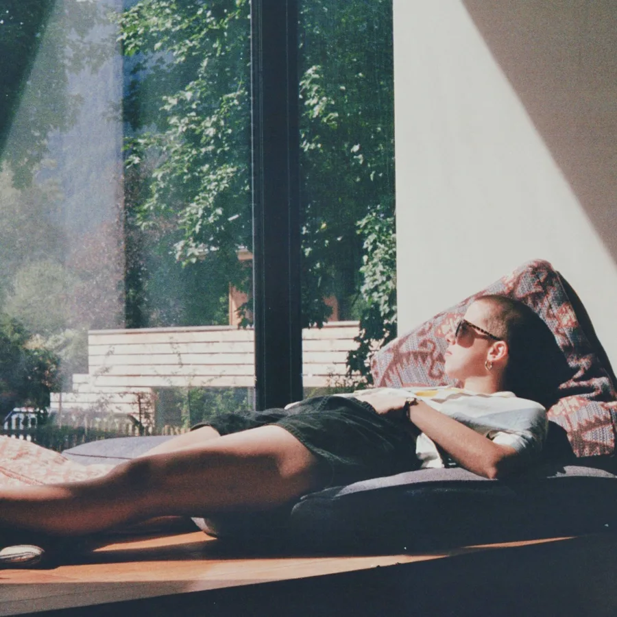 A person lying in the sun beside a large window, arms folded