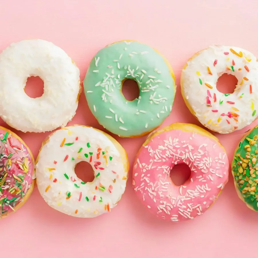 Donuts glaseados de varios colores dispuestos sobre un fondo rosa