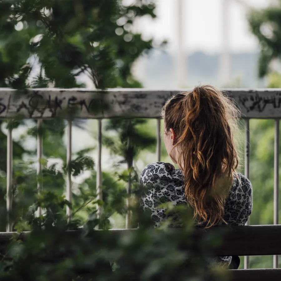 Une personne accoudée à une rambarde, de dos, dans la verdure