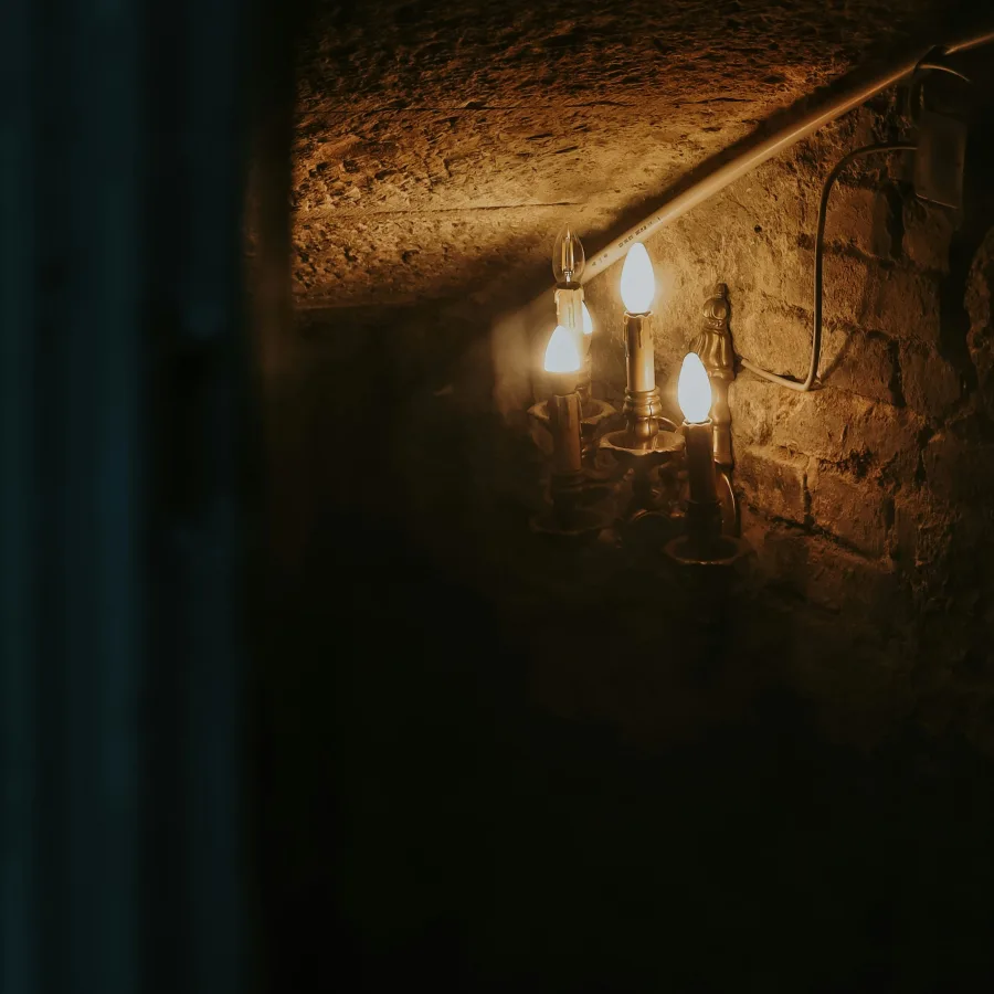 Rincón de un sótano de piedra iluminado por un aplique, el resto de la sala en penumbra