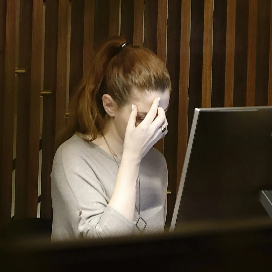 A woman at her workstation, hand on her forehead, in a dimly lit office