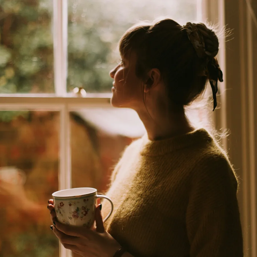 Person standing by a window, a mug held in both hands