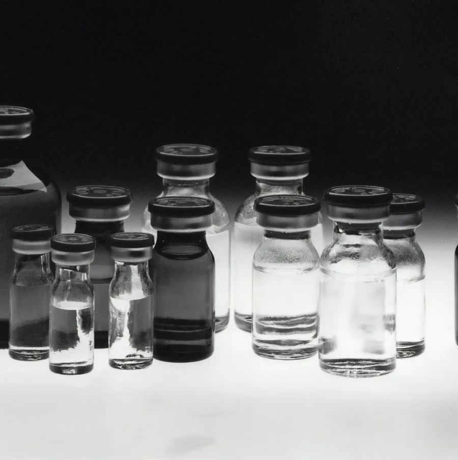 Des flacons de verre alignés sur un fond clair, en noir et blanc