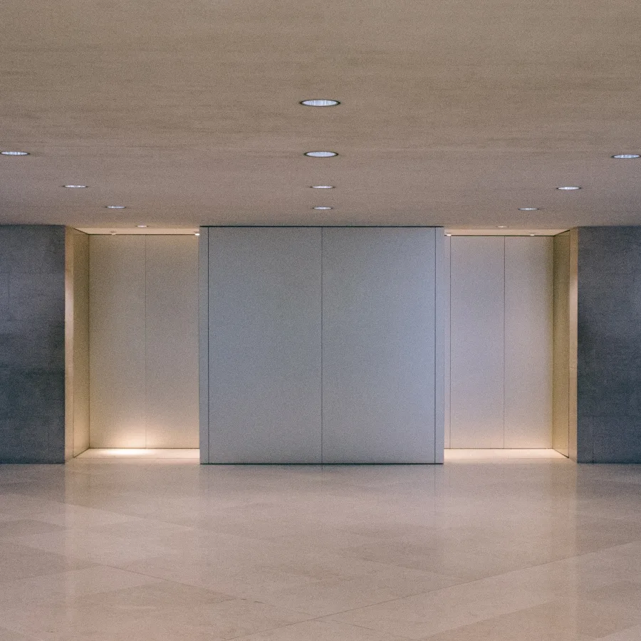 Un vestíbulo de ascensores claro, con las puertas cerradas, bajo una luz suave