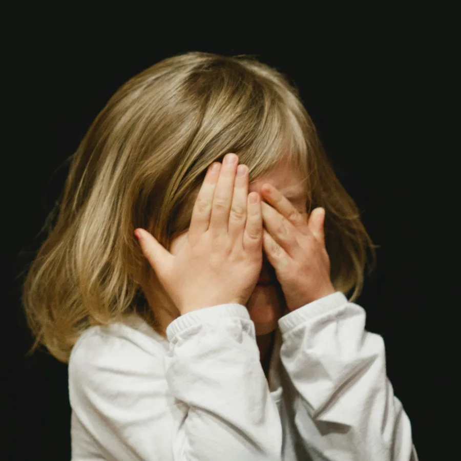 A young child with their face hidden behind their hands