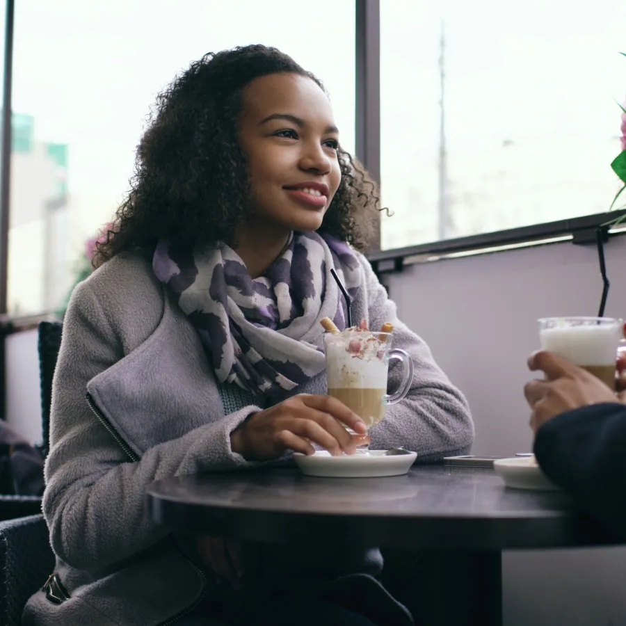 A smiling young woman sitting at a café table, in conversation