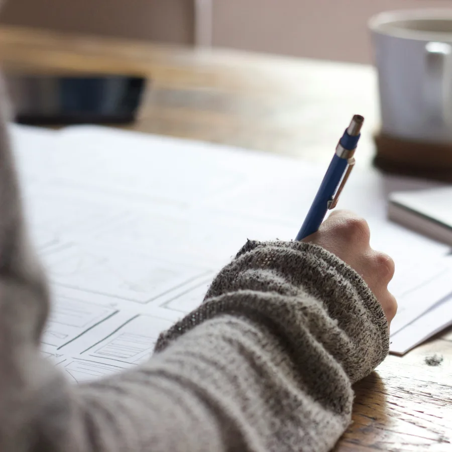 A hand sketching in pencil on a storyboard, beside a mug