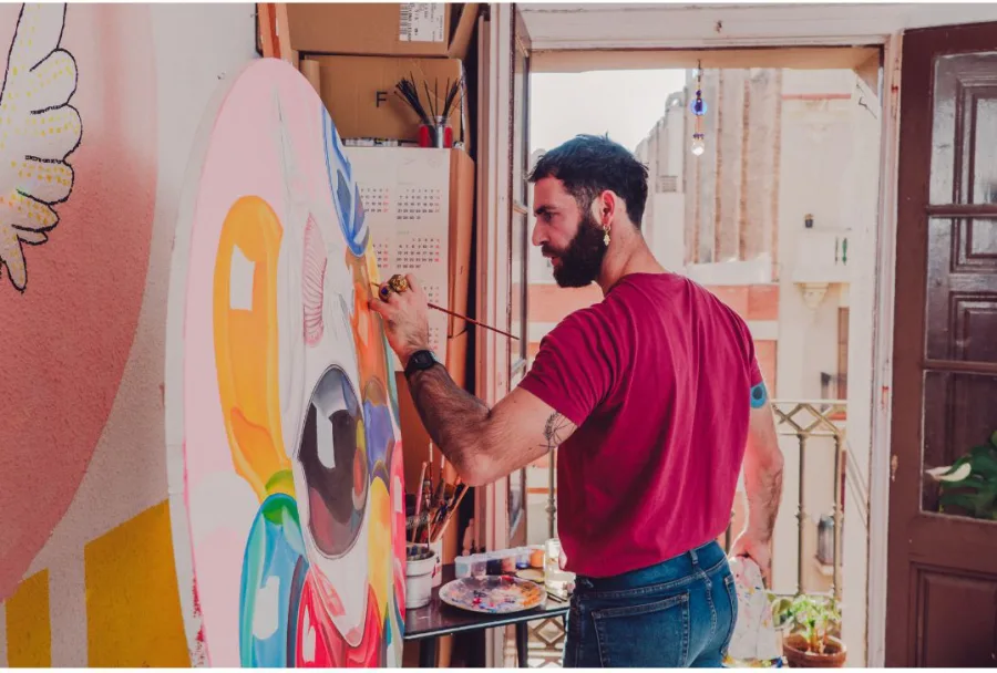 A painter at work on a large colourful canvas, in a studio open to the street