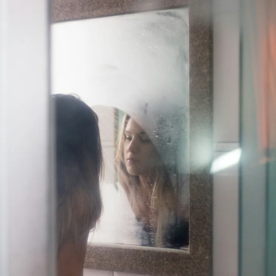 Mujer frente a un espejo empañado, con el reflejo medio borrado por el vaho