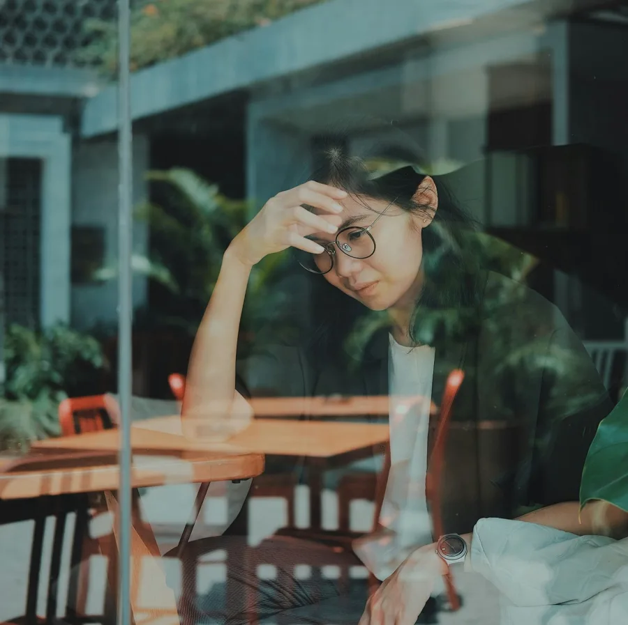 Woman sitting behind a window, hand against her forehead