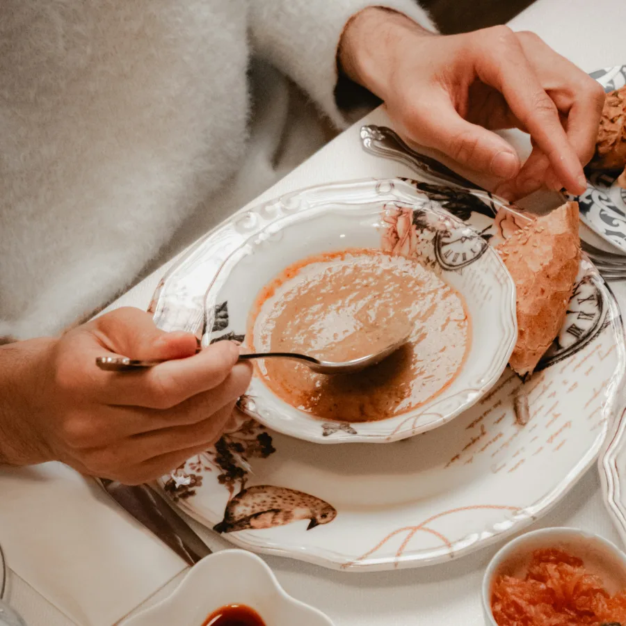 Persona a la mesa, cuchara en mano, ante un plato de sopa casi terminado