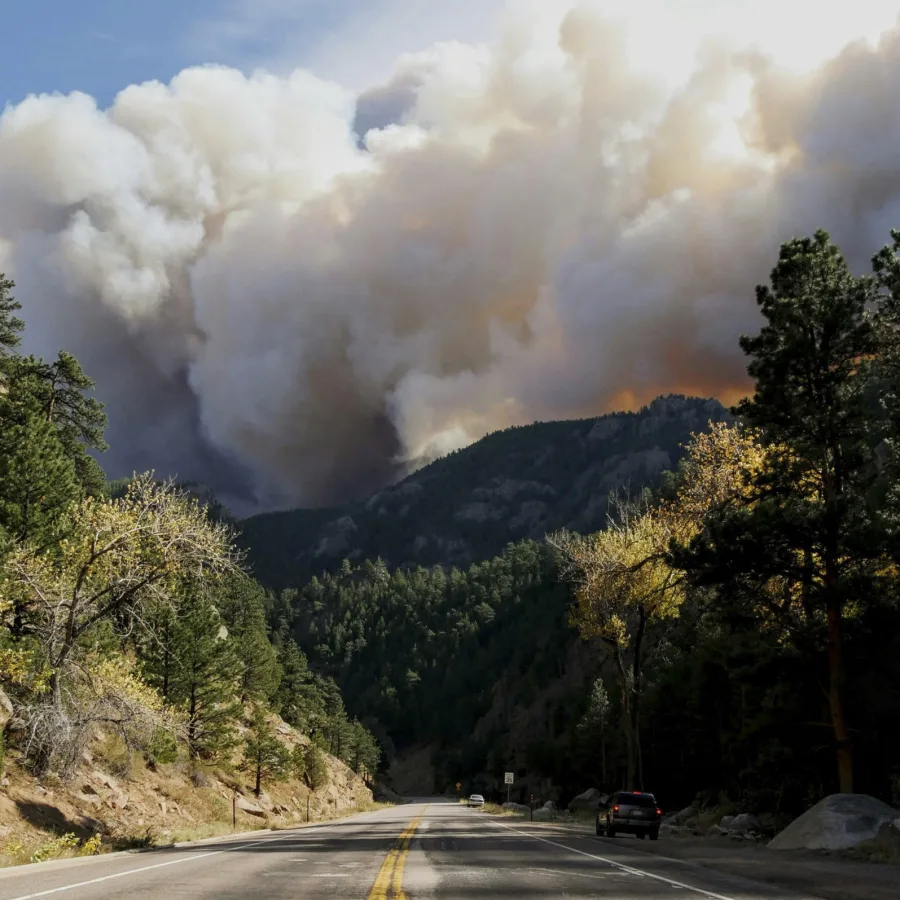 Carretera de montaña bajo una inmensa columna de humo de incendio forestal