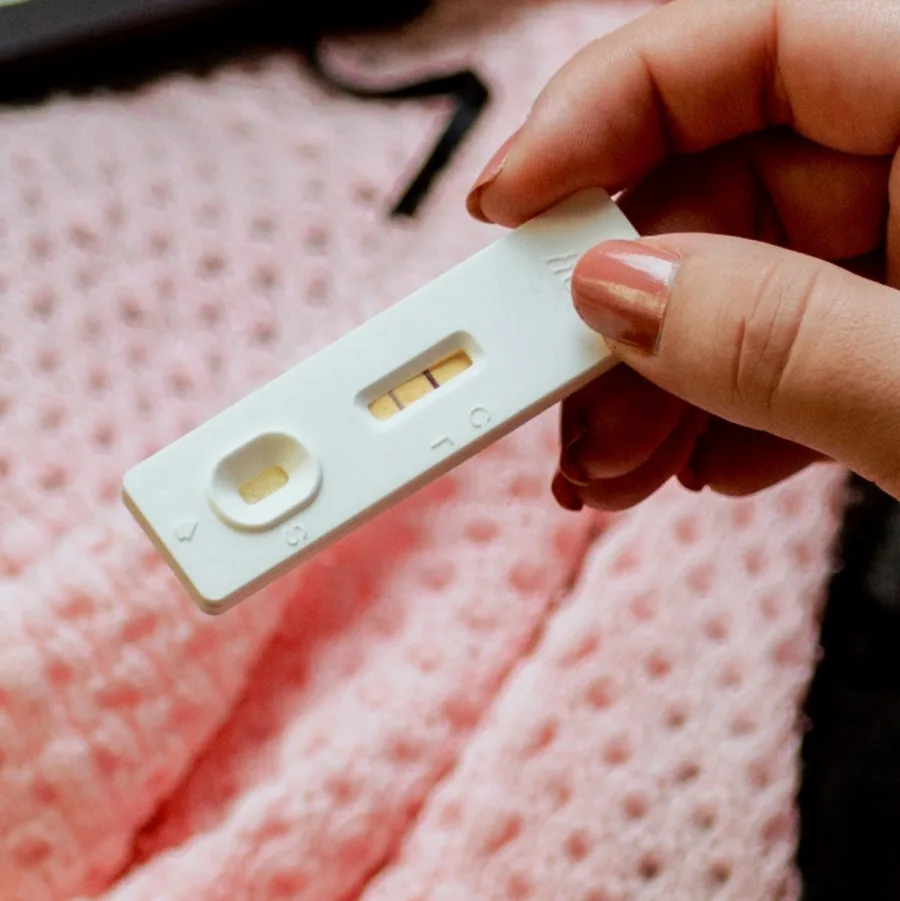 A pregnancy test held in one hand above a pink knitted blanket