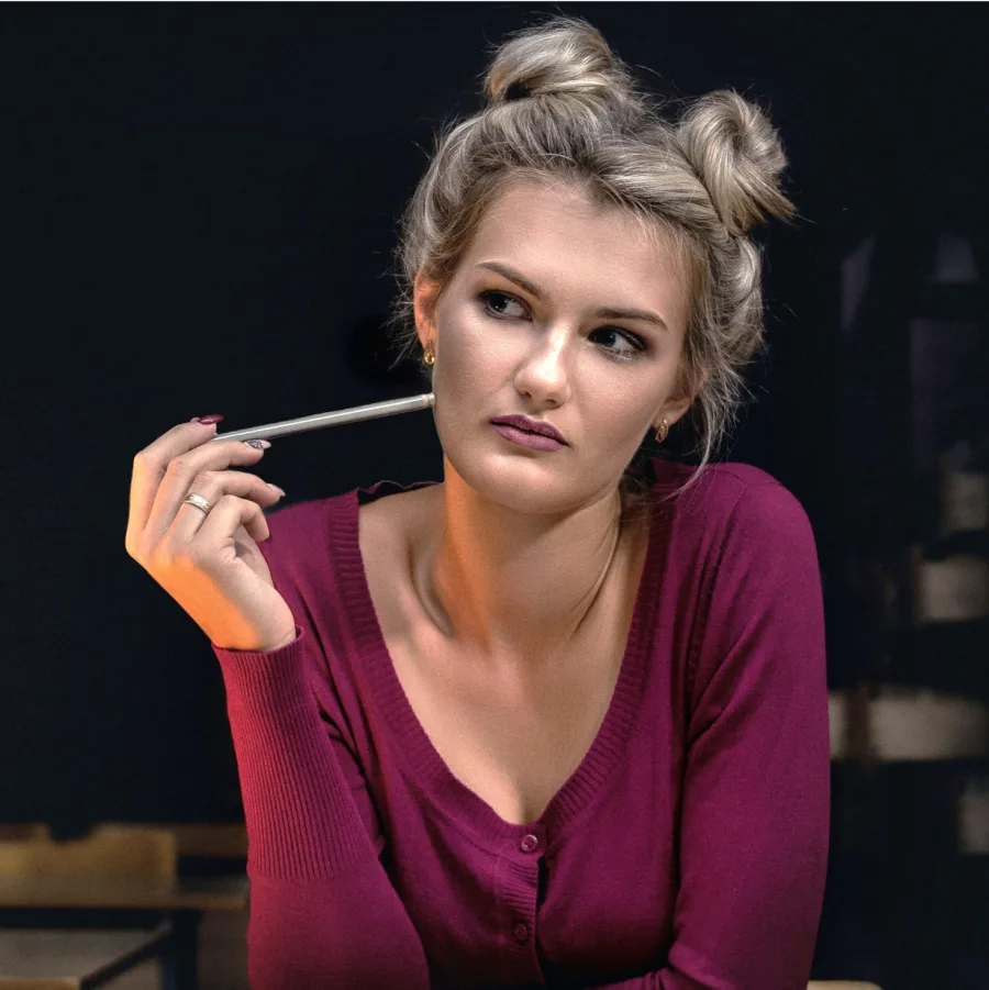 A thoughtful woman holding a pen, her gaze turned to one side