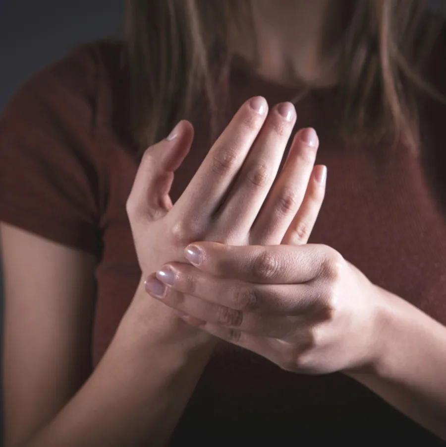 Une femme qui masse lentement sa main, le visage hors du cadre
