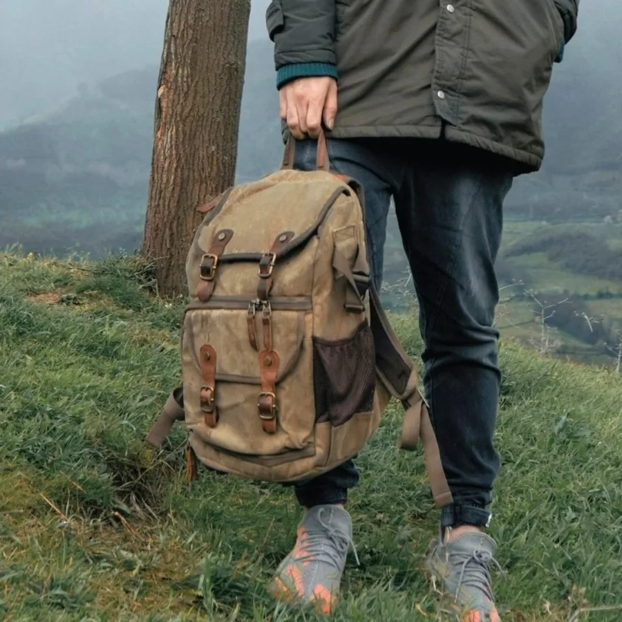 A canvas backpack carried by hand along a grassy path