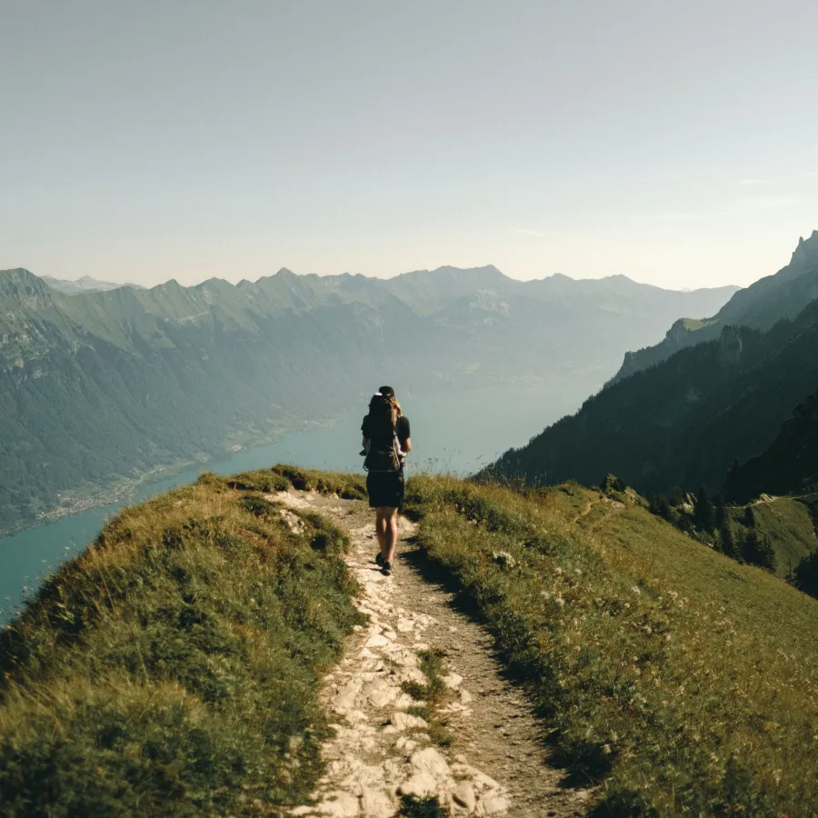 A hiker walking steadily along a ridge path above a lake