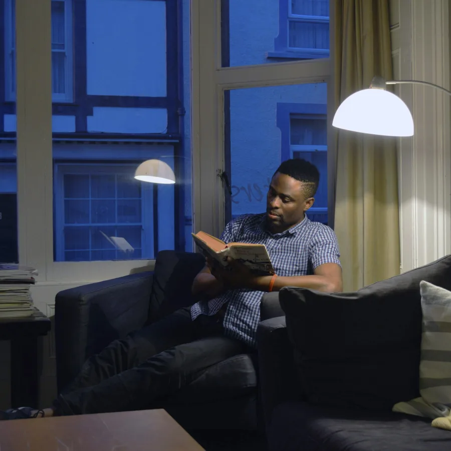 Man alone reading a book in his living room in the evening