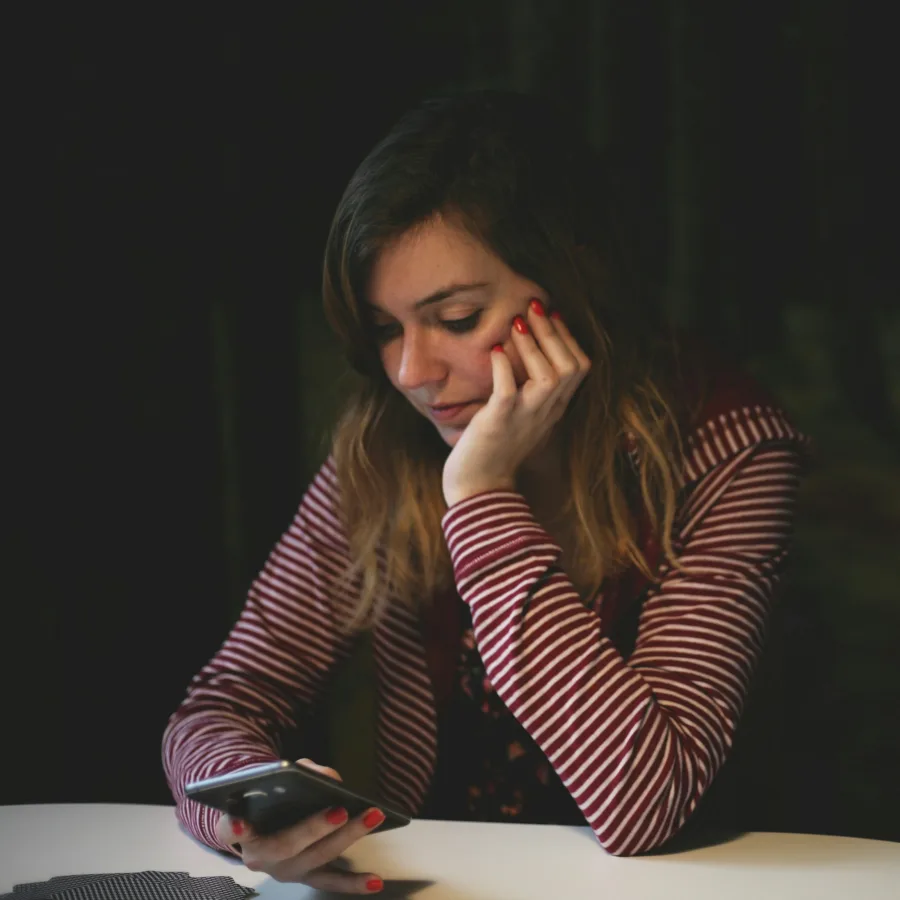 Young woman alone at a table, looking at her phone