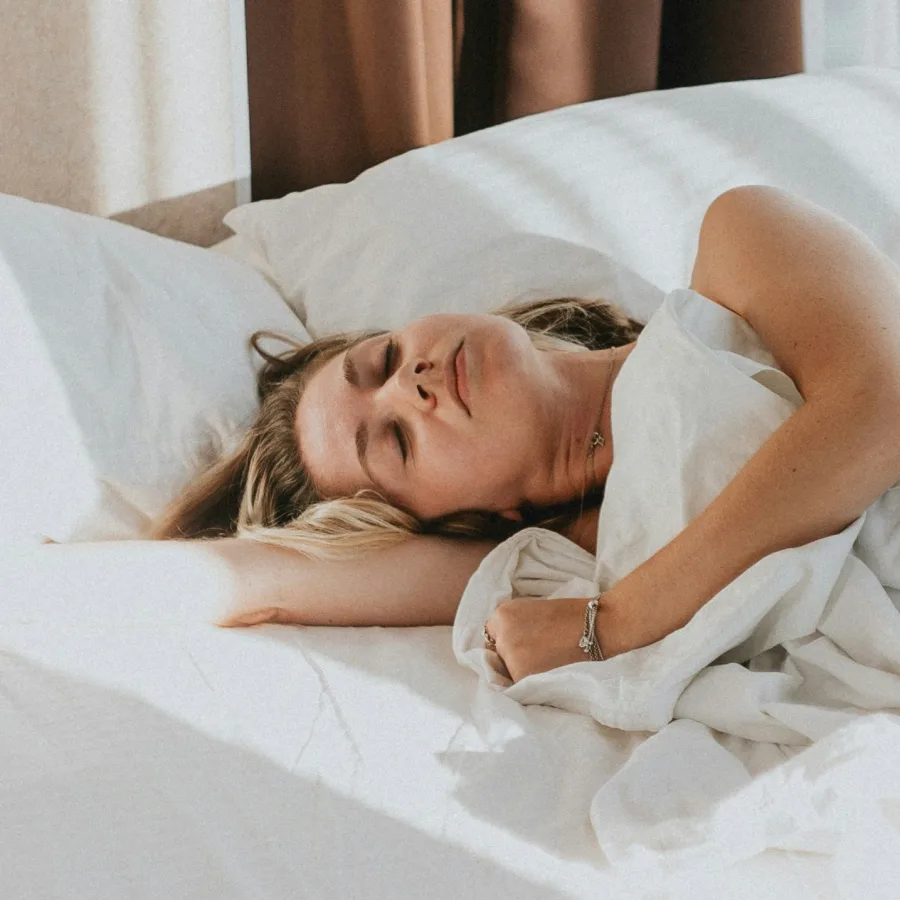 Mujer acostada en una cama clara, con los ojos cerrados, con luz suave