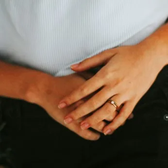 Clasped hands resting at the waist, over a white top and black trousers