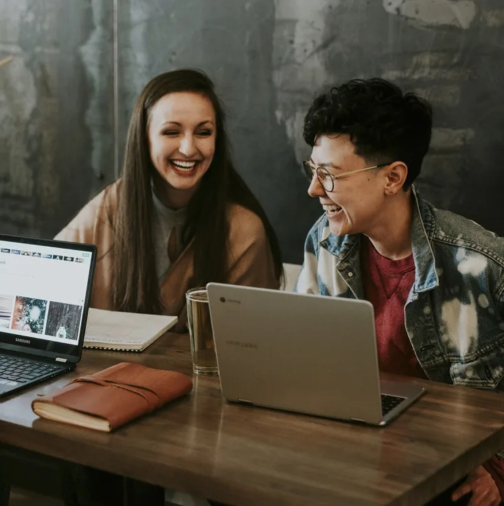Two colleagues laughing in front of their laptops