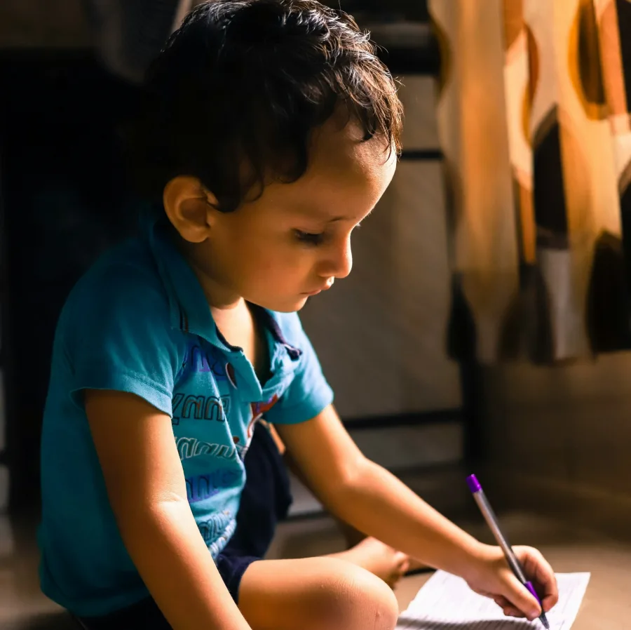Young child sitting, absorbed, writing on a sheet of paper
