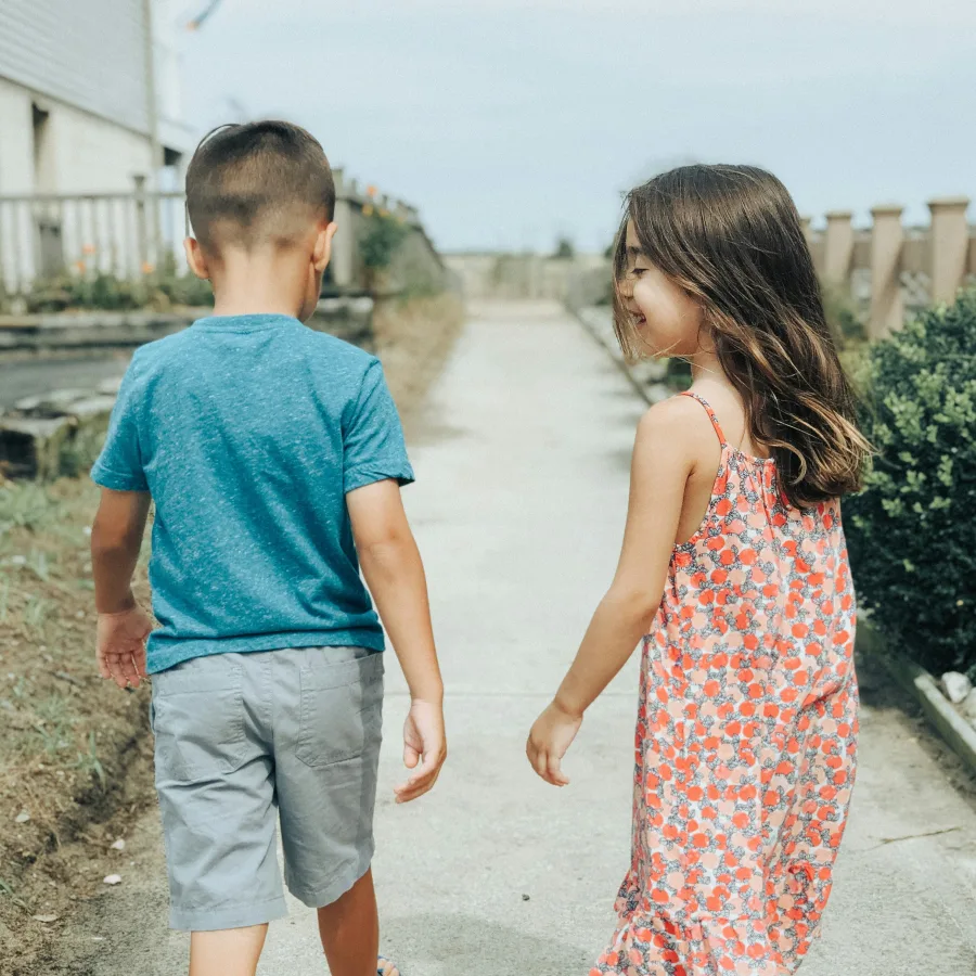 Two children side by side on a path, one turning towards the other