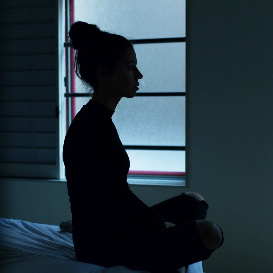 Femme assise sur son lit au milieu de la nuit, silhouette devant une fenêtre bleutée