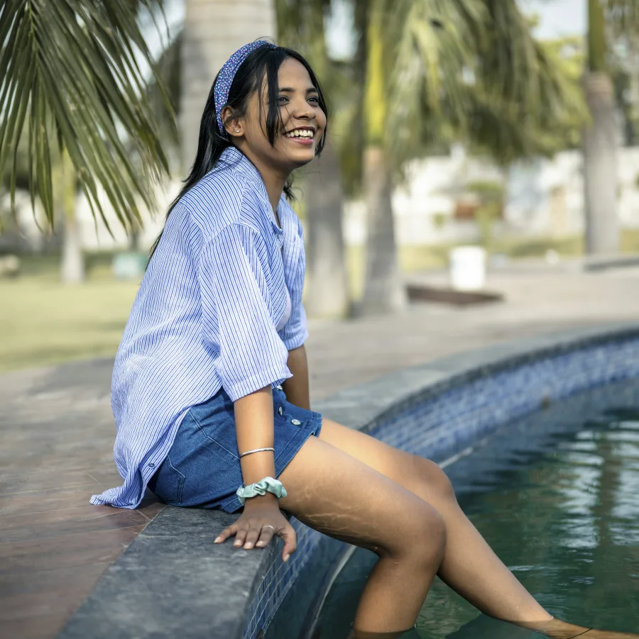 Mujer sonriente sentada al borde de una piscina, con los pies en el agua