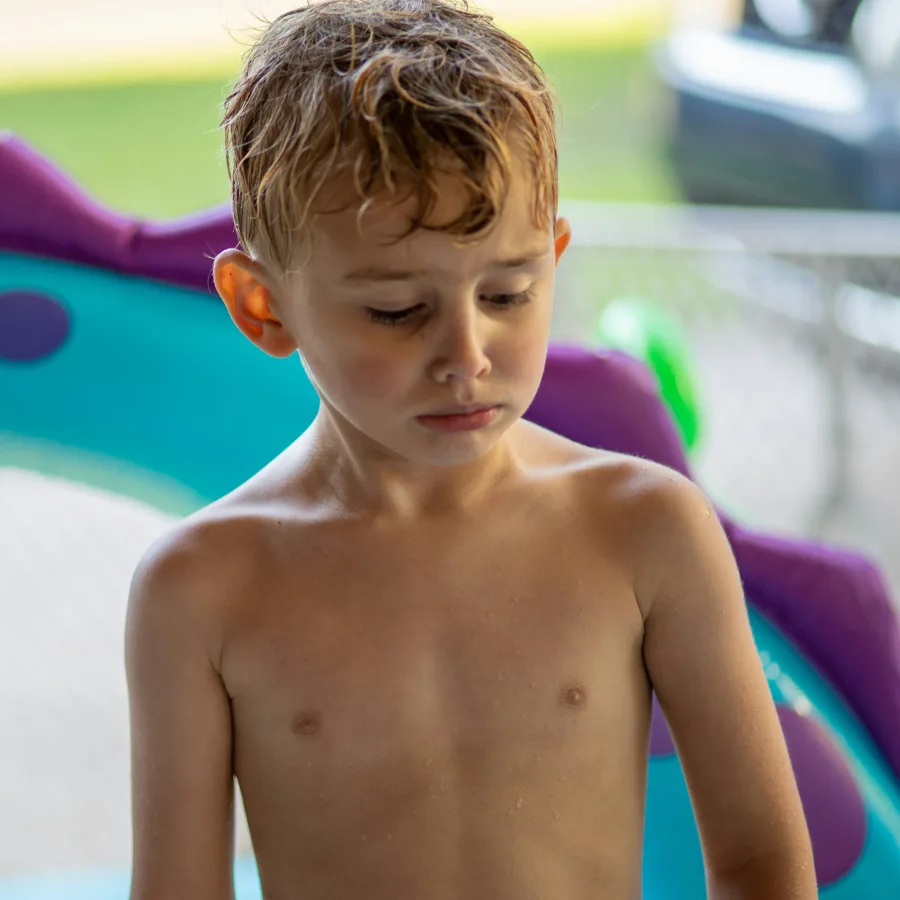 Young boy with wet hair, looking down, at the edge of a swimming pool