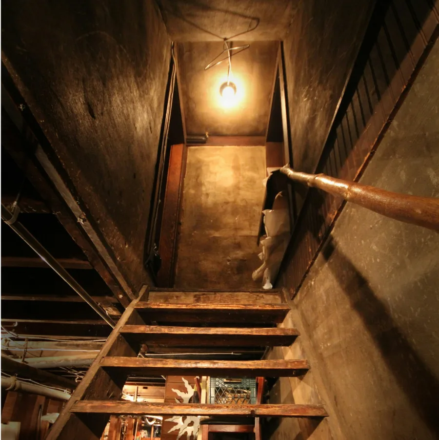 Escalera de sótano de madera vista desde arriba, iluminada por una bombilla desnuda