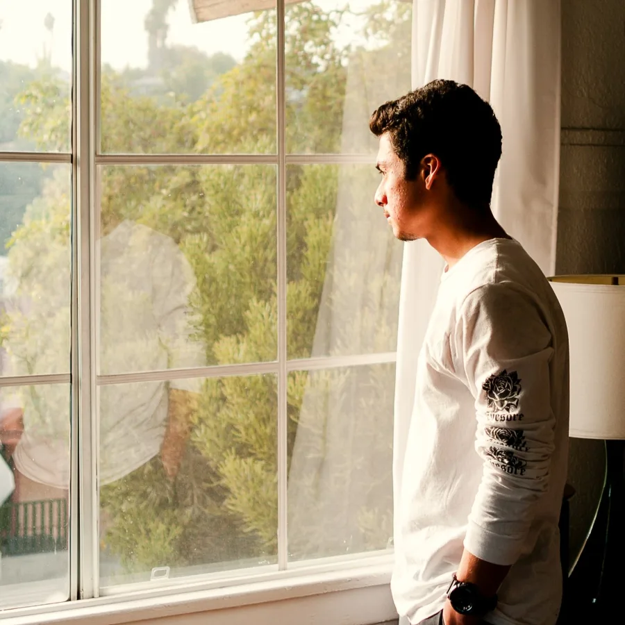 Man standing at a window, looking out at the greenery in the garden