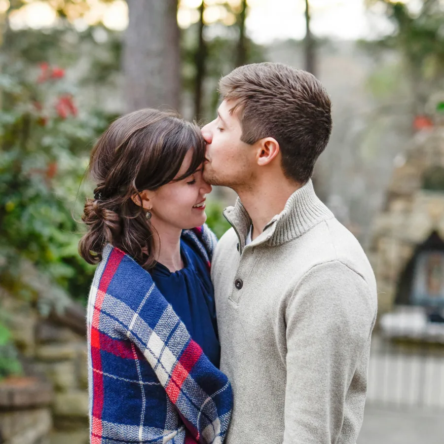 A man kissing his partner's forehead, outdoors, in autumn light