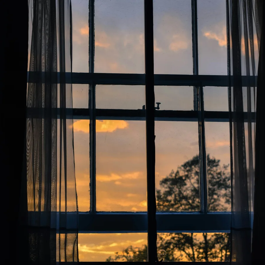 A bedroom window in the early morning, curtains drawn across an orange sky