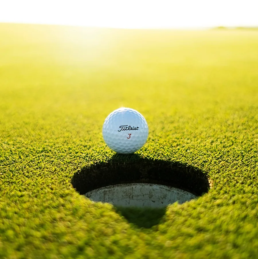 Golf ball sitting on the lip of the hole on a side-lit green