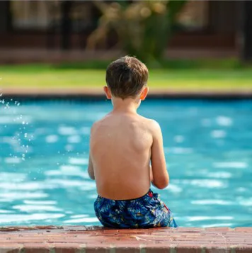 Child sitting with their back to us at the edge of a pool, feet in the water