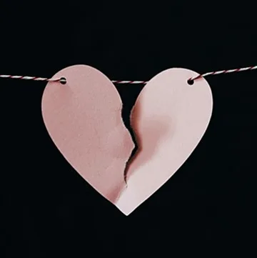 A pink paper heart torn in two, hanging from a string against a black background