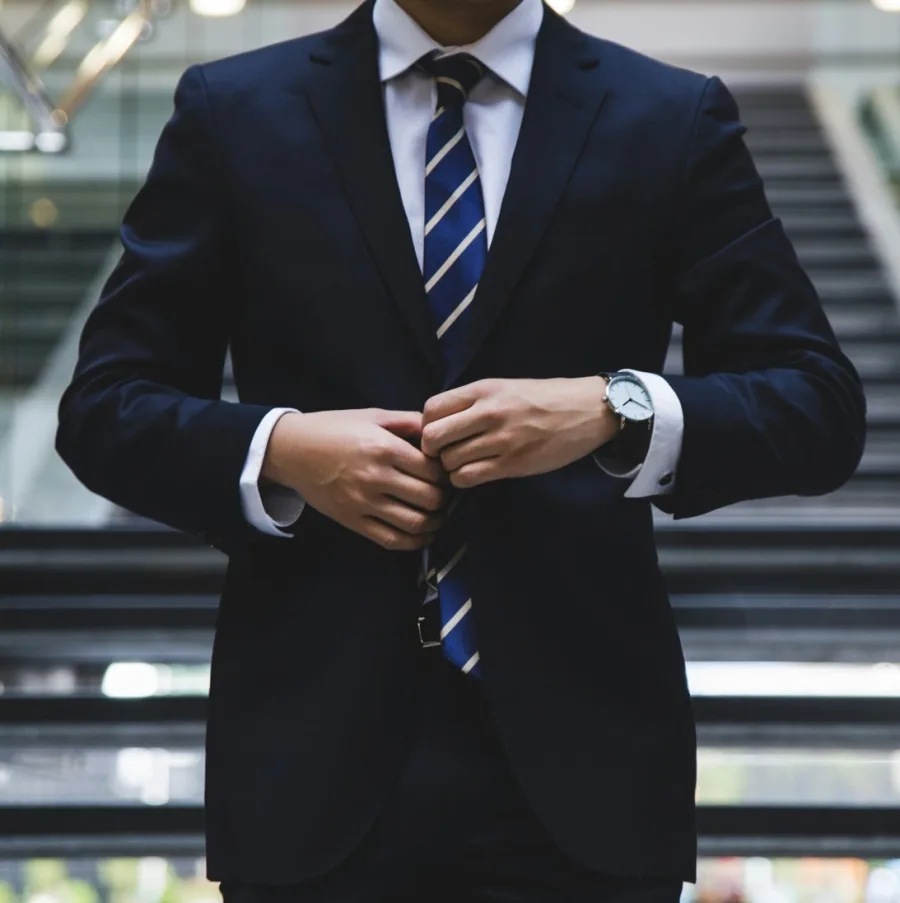 Someone in a suit buttoning their jacket in front of an office staircase