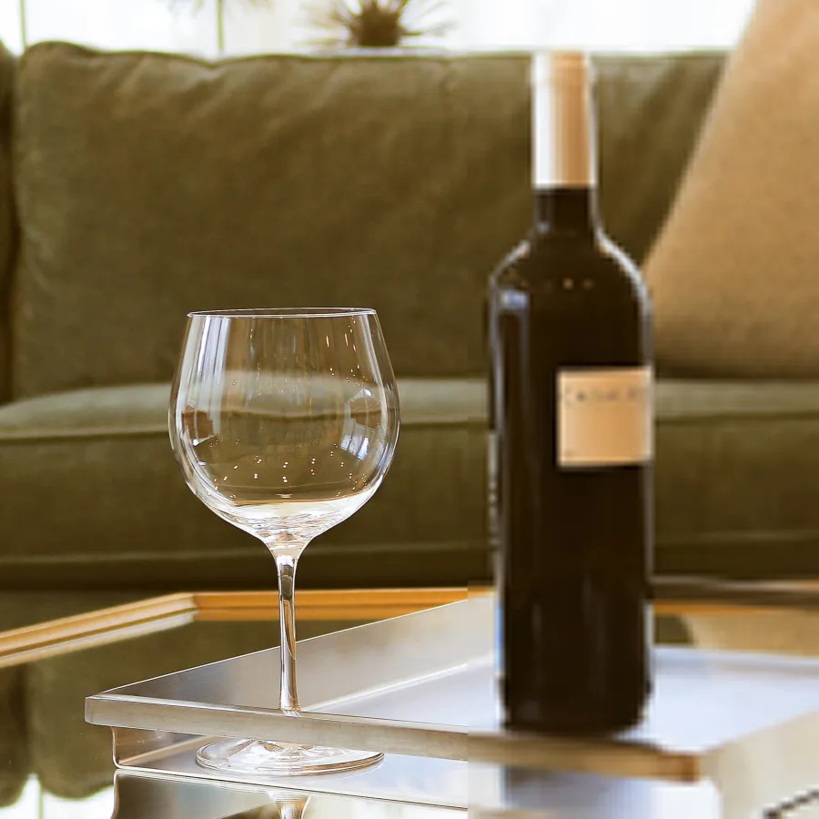 A wine bottle and an empty glass on a side table at the end of the day