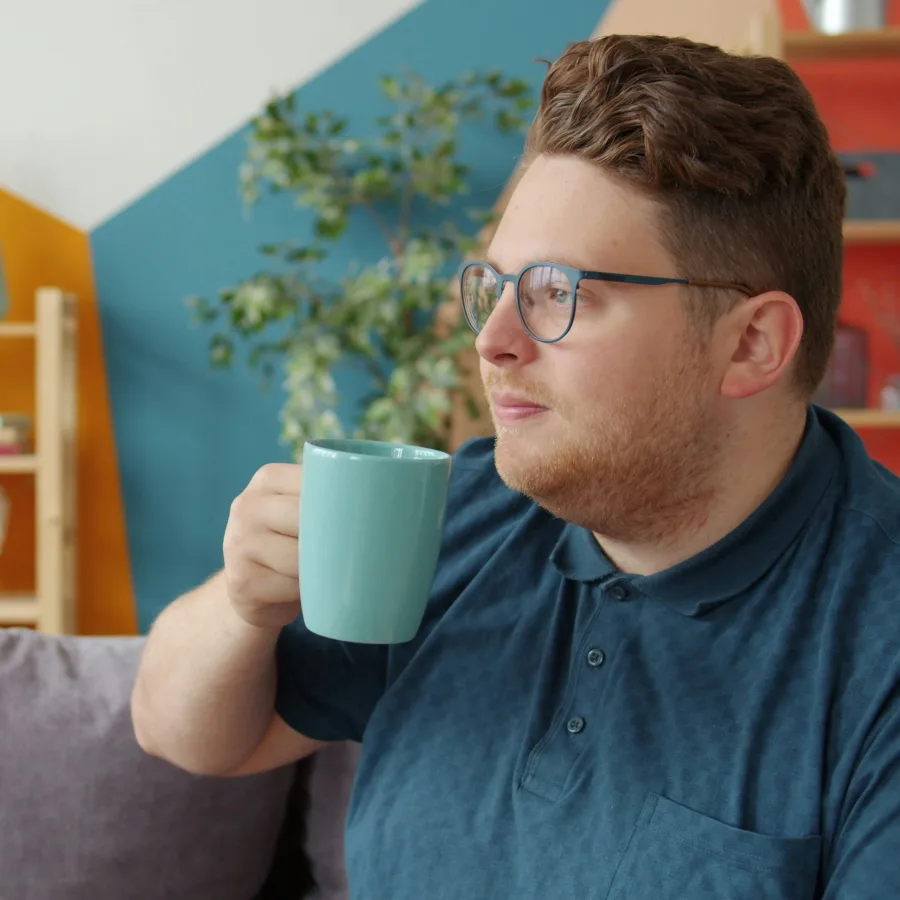 A man sitting at home holding a mug, looking into the distance