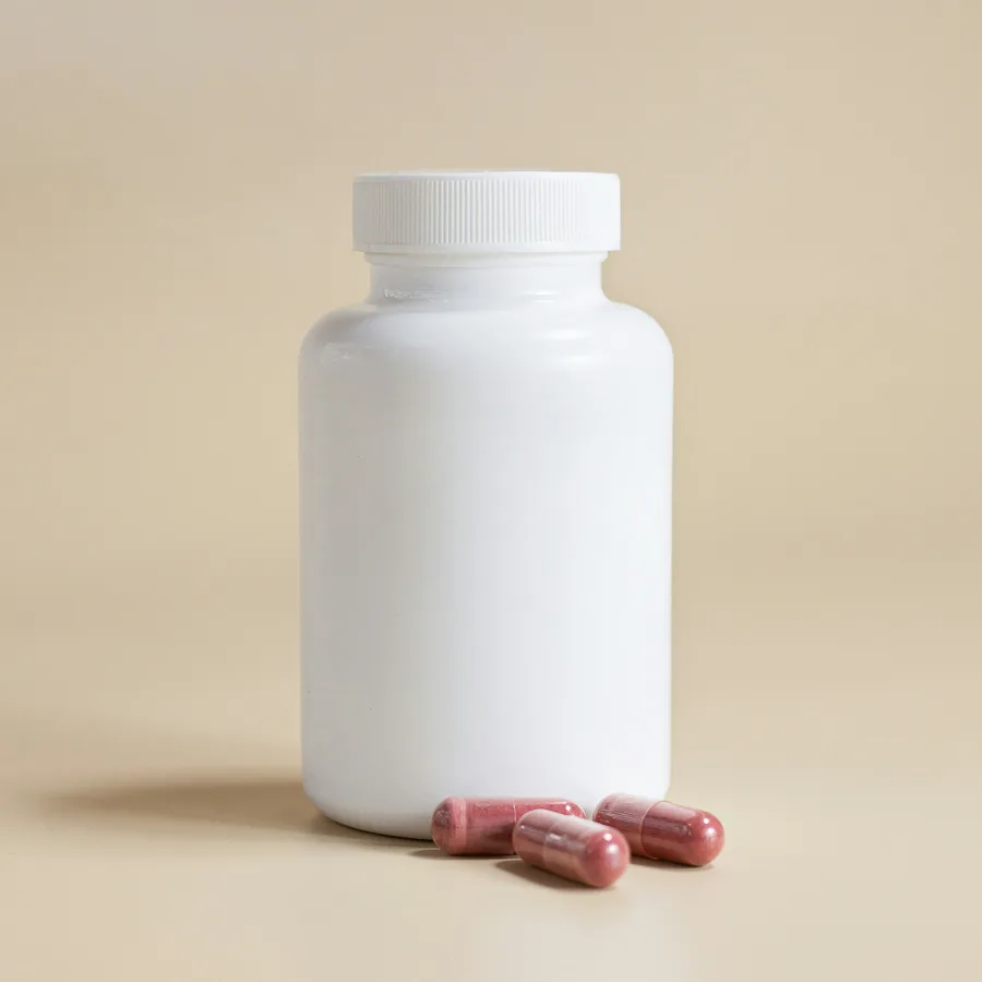 A white bottle and three capsules on a beige background