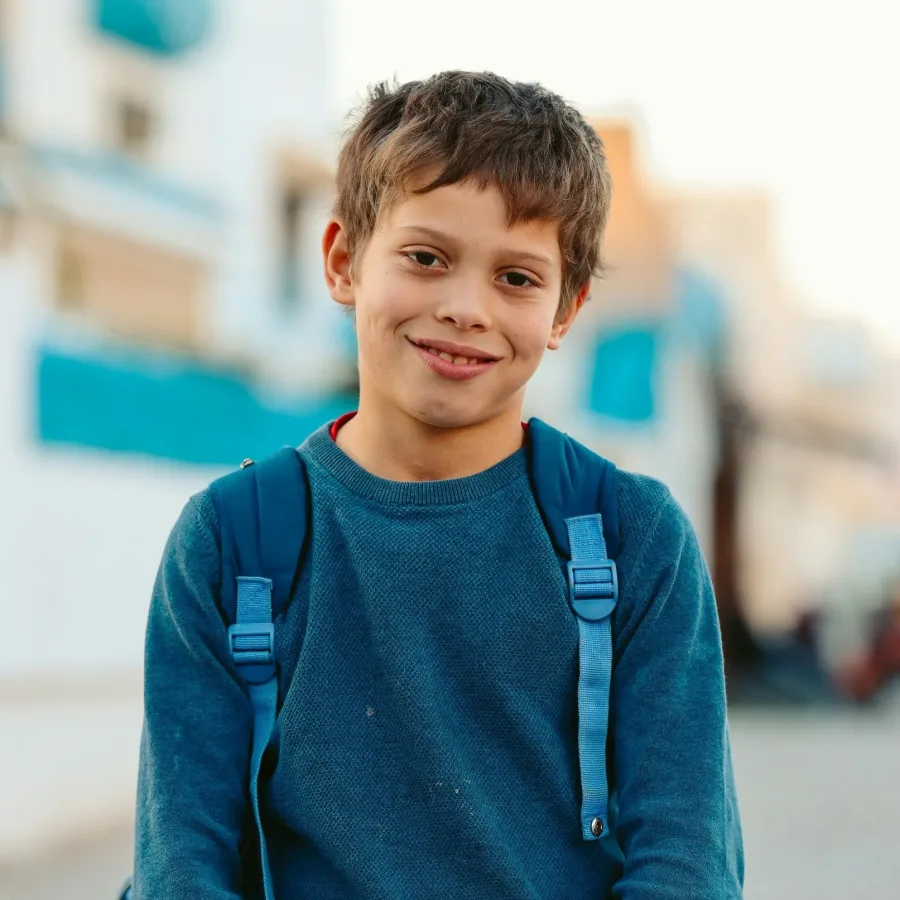 Niño sonriente en la calle, con las correas de la mochila sobre los hombros