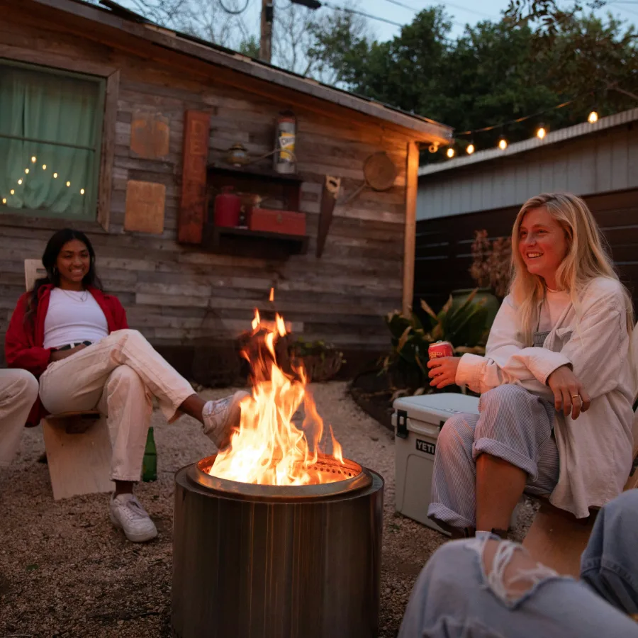 Two friends sitting around a fire in a yard at dusk