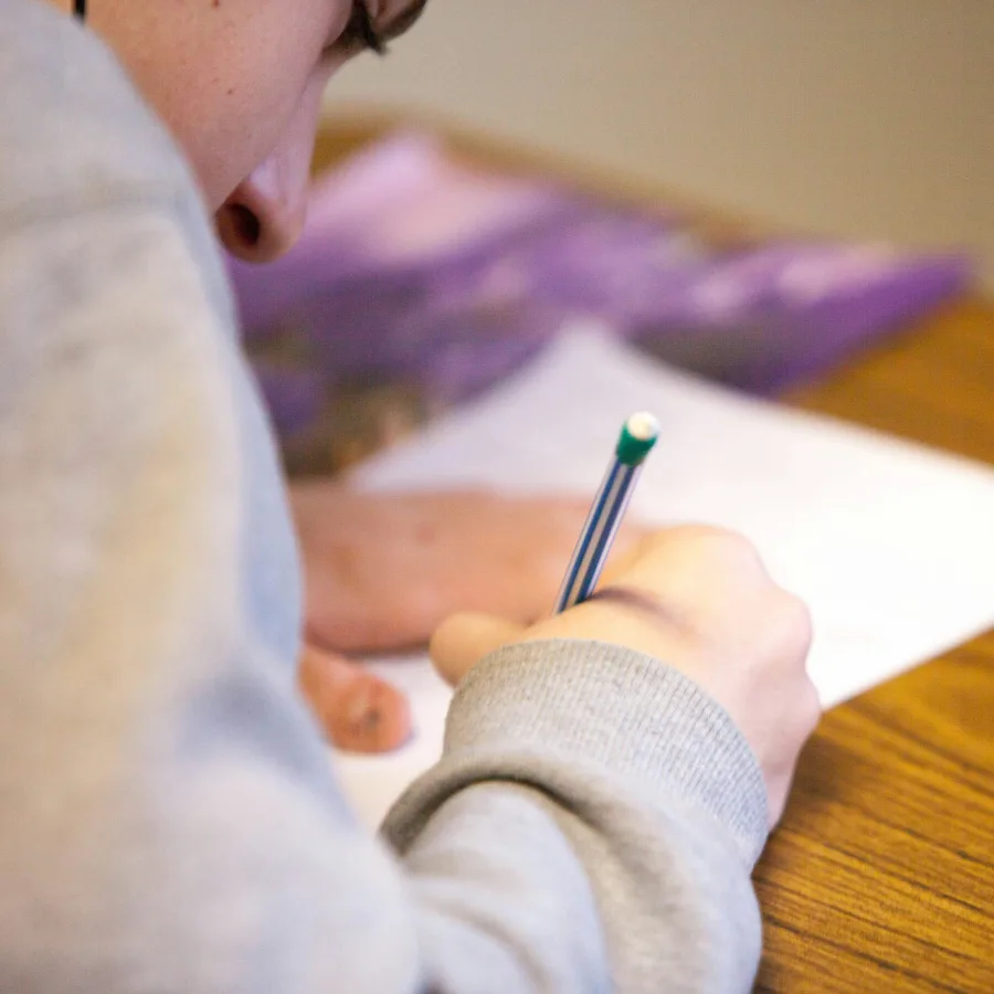 A student's hand holding a pen above a page that has stayed blank