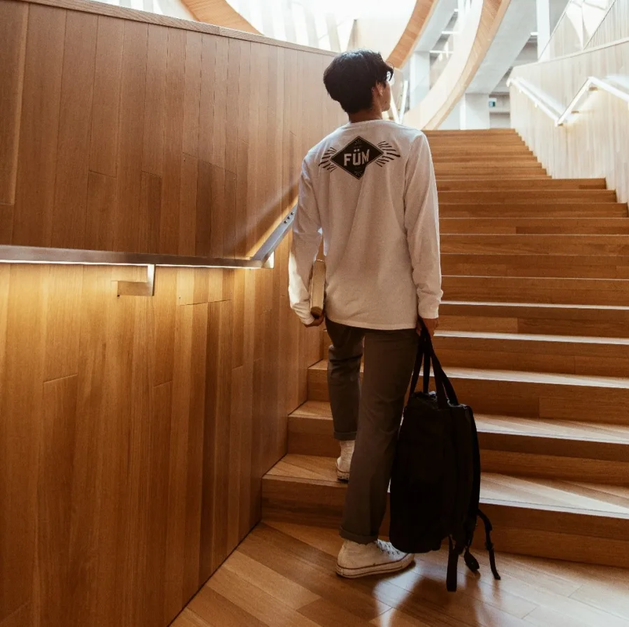Teenager seen from behind, bag on one shoulder, leaving a school building at the end of the day