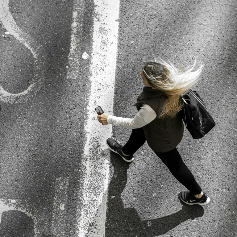 A woman walking briskly down the street, phone in hand, seen from above