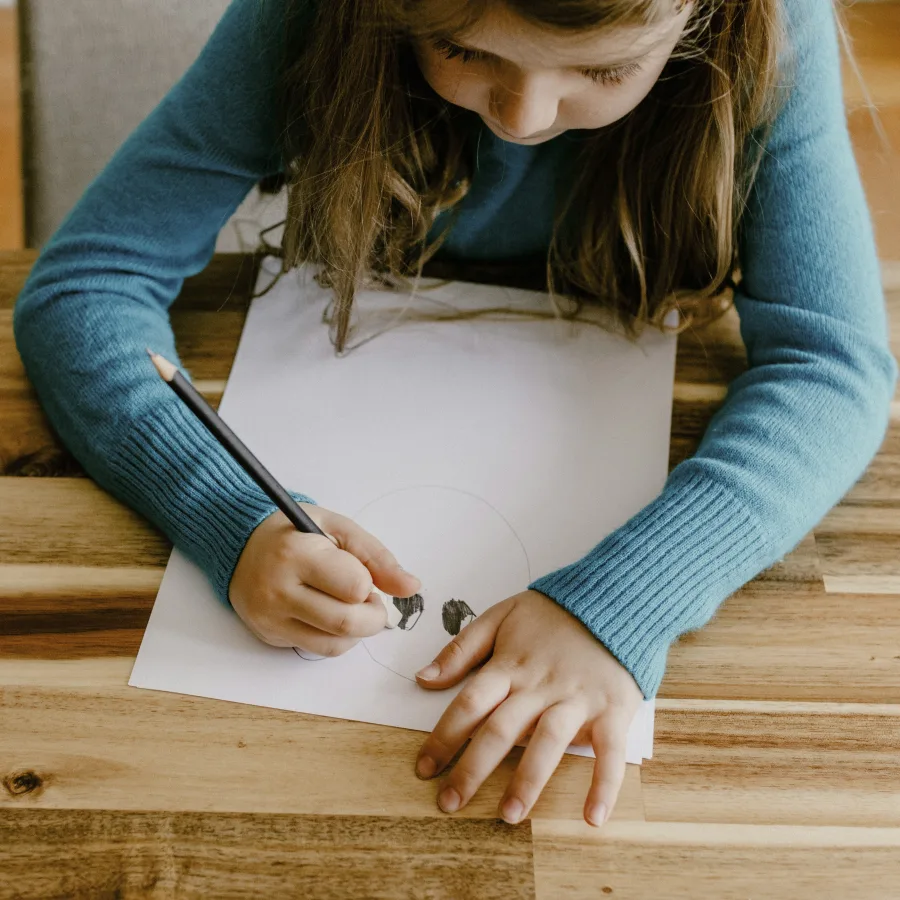 A girl leaning over a sheet of paper, absorbed in a pencil drawing