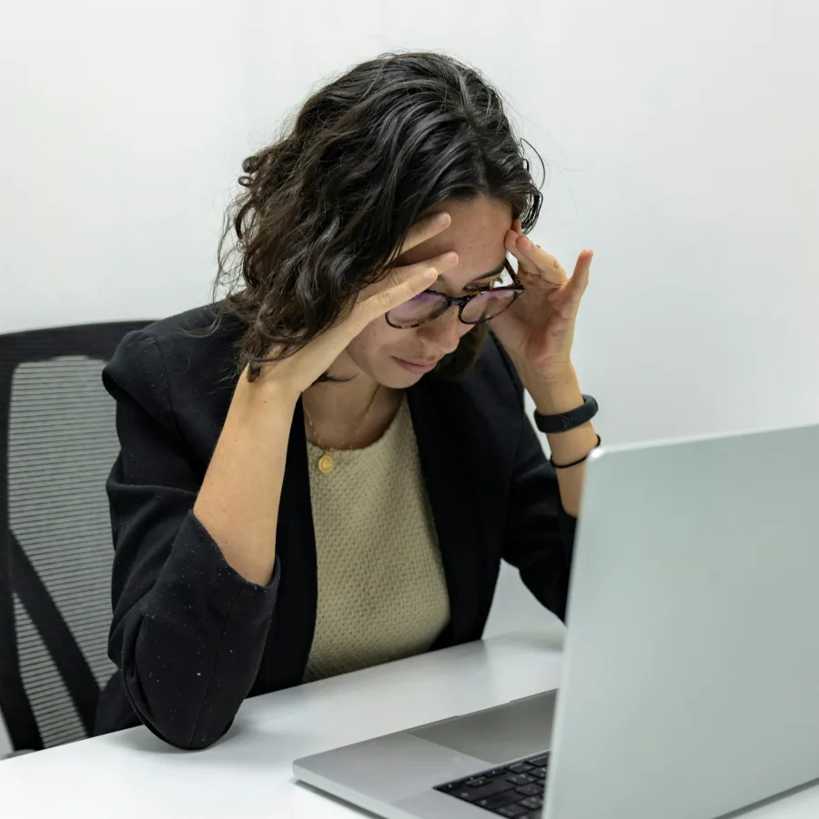 A woman sitting at a laptop, hands at her temples