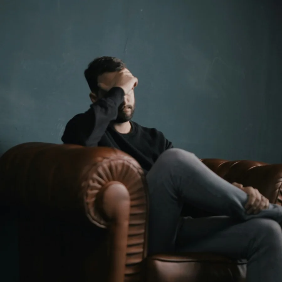 Man sitting on a sofa, hand across his brow, in a dim room